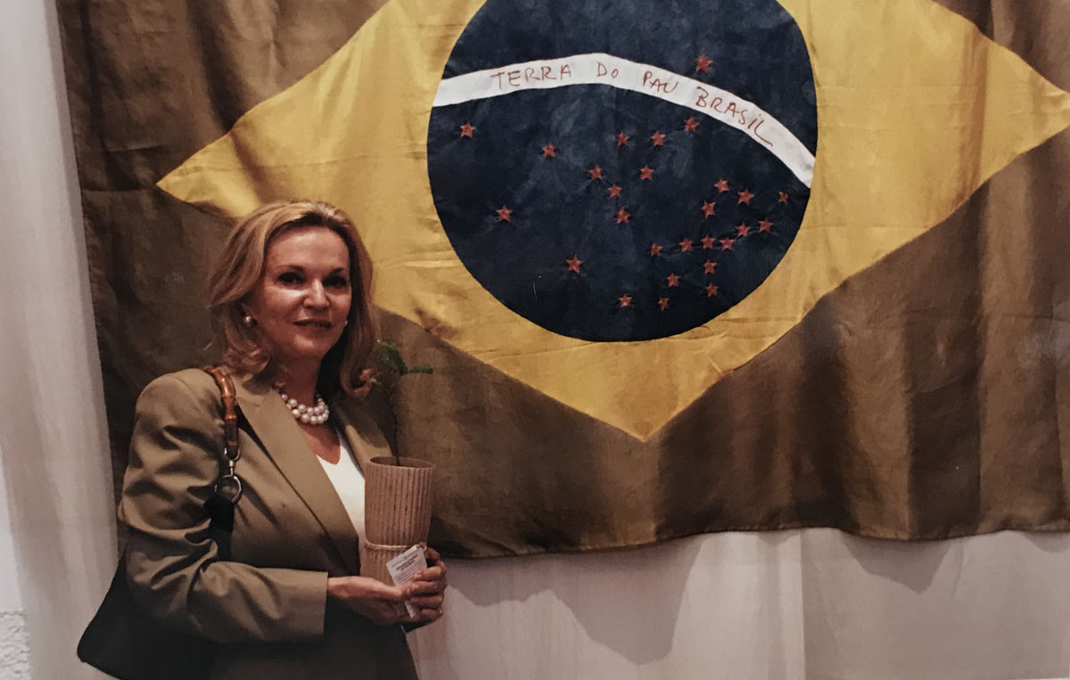 Ana Maria Vieira Santos em frente à bandeira bordada com fios de seda e tingida com corantes do Pau-Brasil